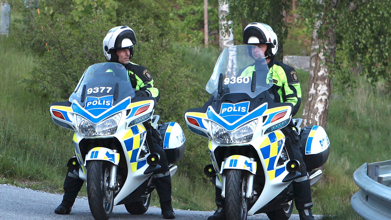 Kaksi ruotsalaista moottoripy&ouml;r&auml;poliisia partiossa maantien laidassa, taustalla vihre&auml;&auml; mets&auml;&auml;.